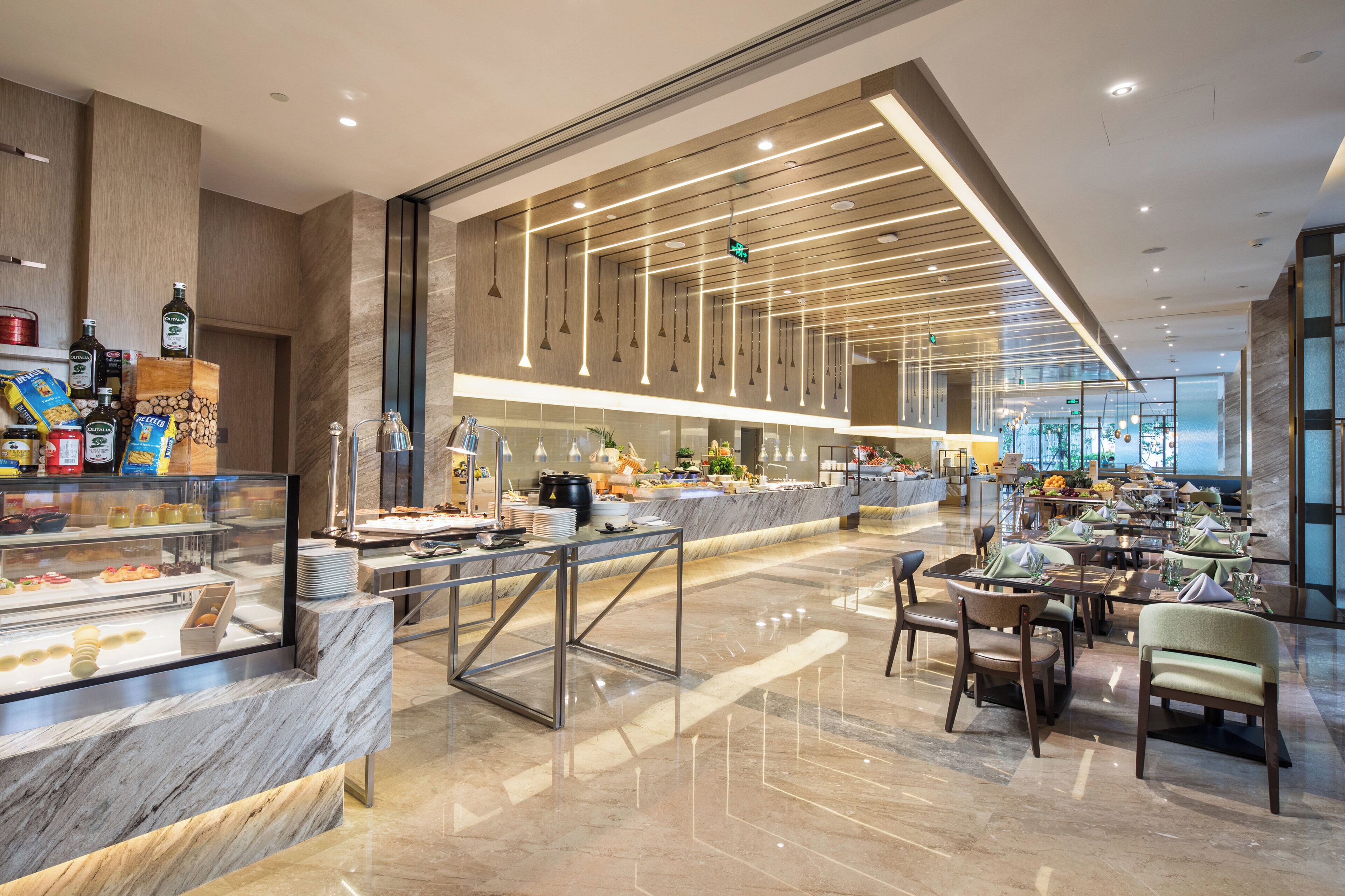 A modern hotel lobby with a marble reception desk, a buffet area, and a seating area with tables and chairs.