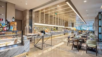 A modern hotel lobby with a marble reception desk, a buffet area, and a seating area with tables and chairs.