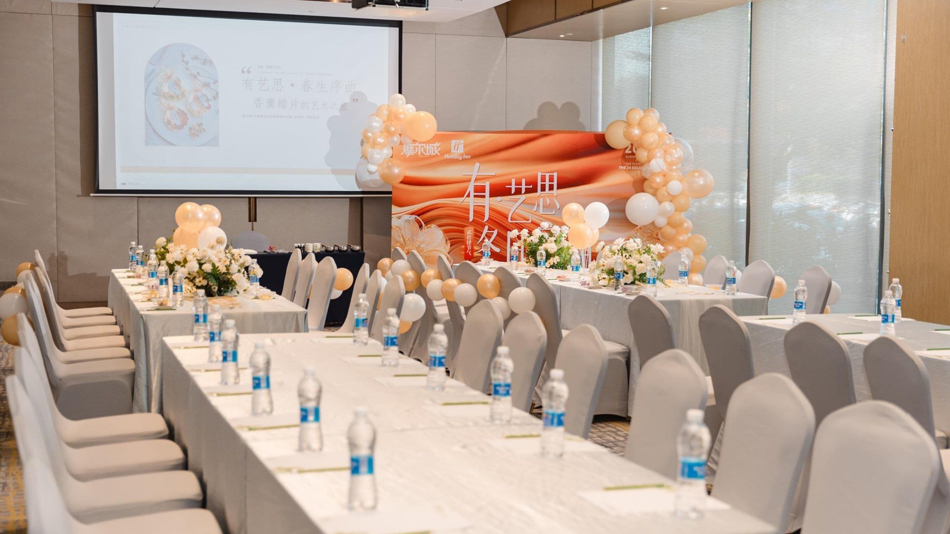 A conference room with tables set for a meeting, chairs arranged in rows, and a projection screen in the background.