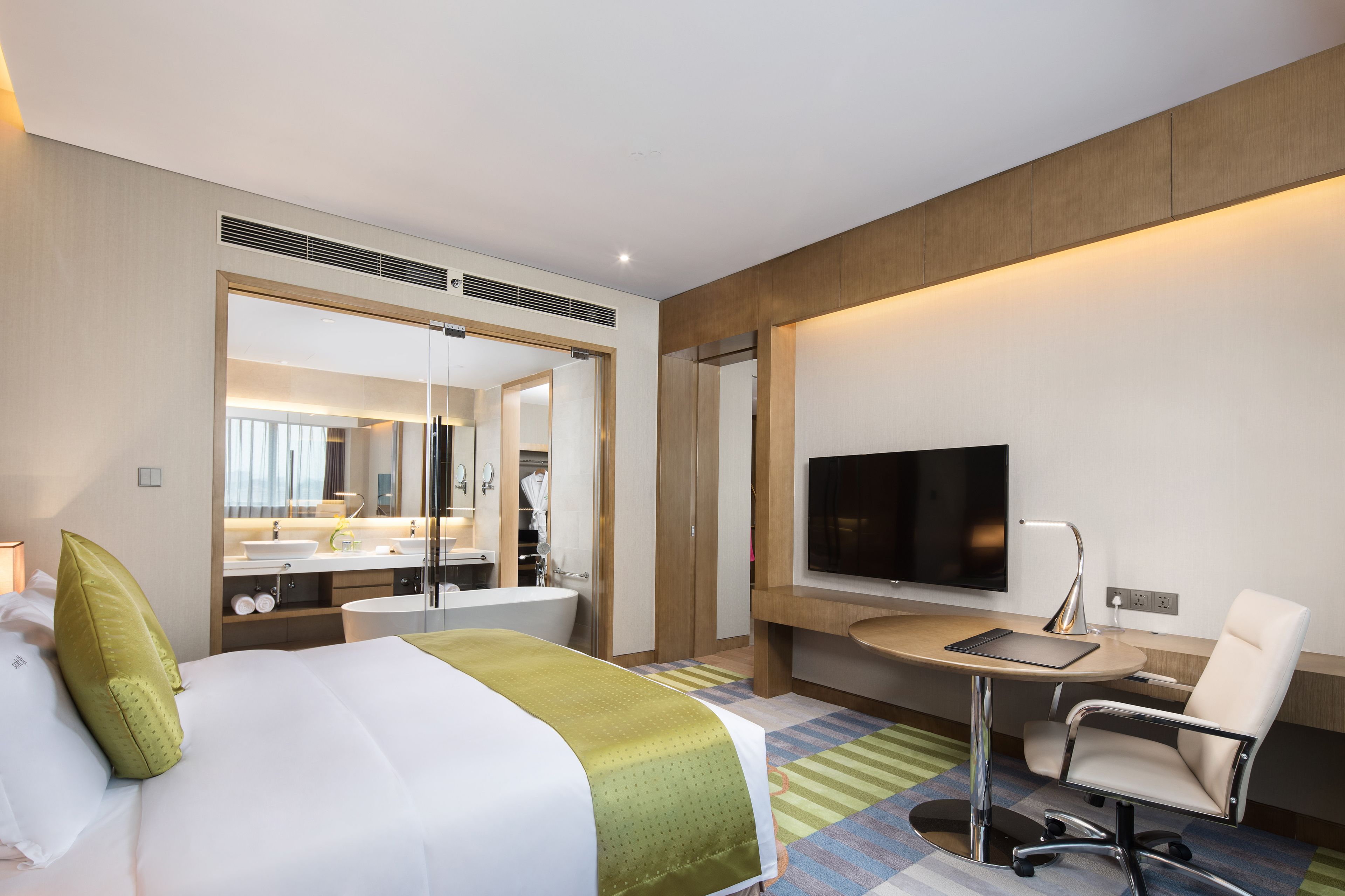 Habitación de hotel con cama, escritorio, silla, televisor y baño visible a través de una puerta abierta.