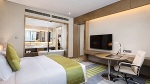 Une chambre d’hôtel avec un lit, un bureau, une chaise, une télévision et une salle de bain visible à travers une porte ouverte.
