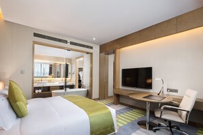 A hotel room with a bed, a desk, a chair, a television, and a bathroom visible through an open door. - Holiday Inn Shaoguan Downtown by IHG (Shaoguan)