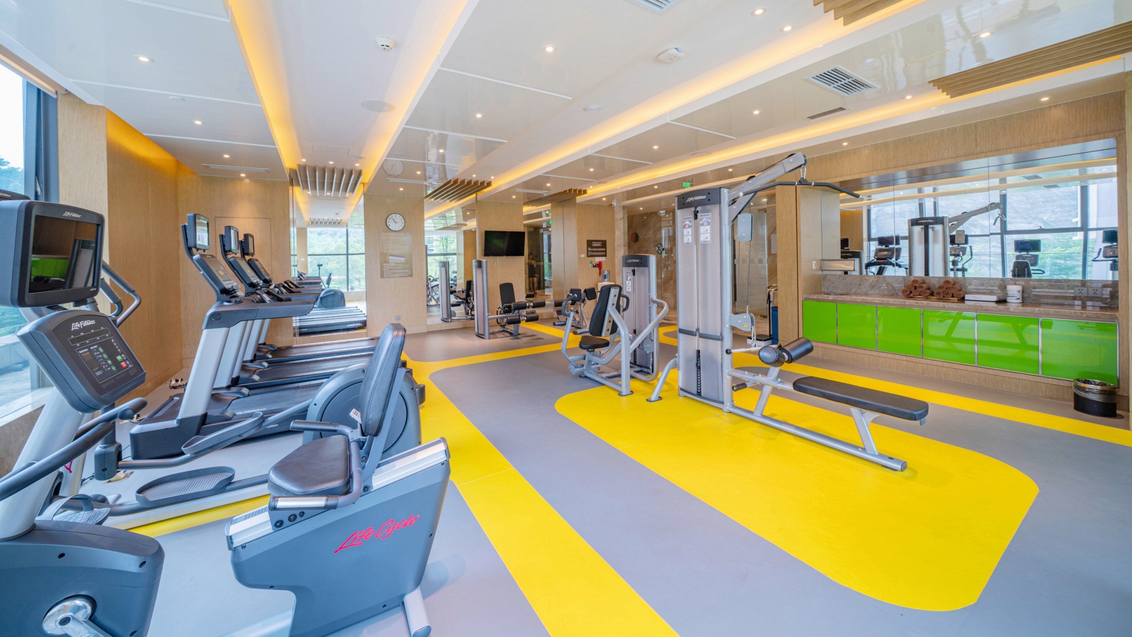 A modern gym with treadmills, weight machines, and a bright yellow floor.