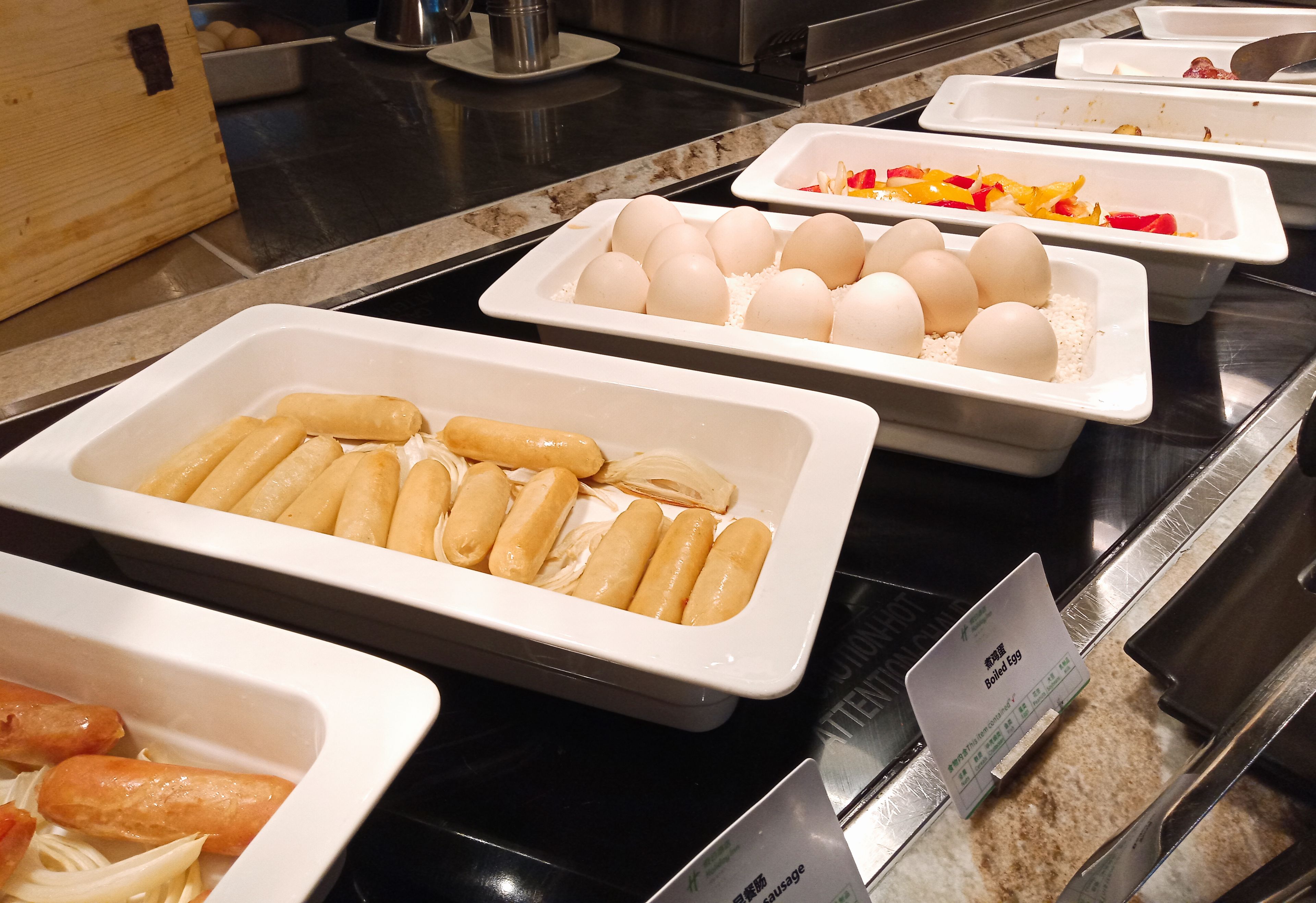 A buffet with various food items including sausages, boiled eggs, and a sign indicating 'Chinese Sausage'.