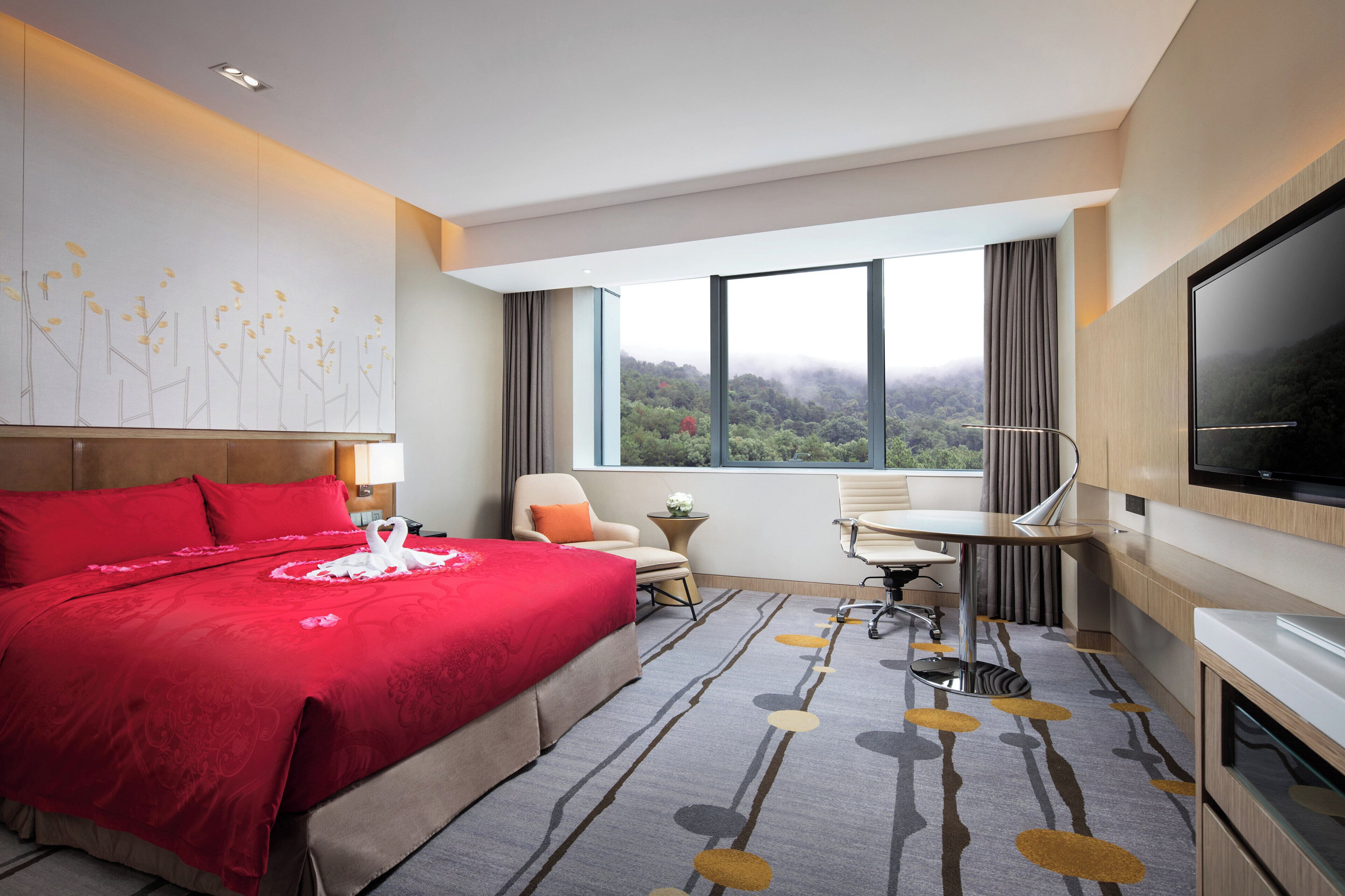 A hotel room with a large bed, a desk, a chair, and a TV.