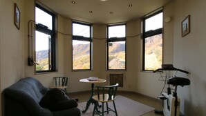 A corner room with a view of mountains, a couch, a table with chairs, and a treadmill. - Petit Resort Hotel Der Barte (Yamagata)
