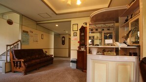 A lobby with a brown leather sofa, a reception desk, and a wall-mounted clock. - Petit Resort Hotel Der Barte (Yamagata)