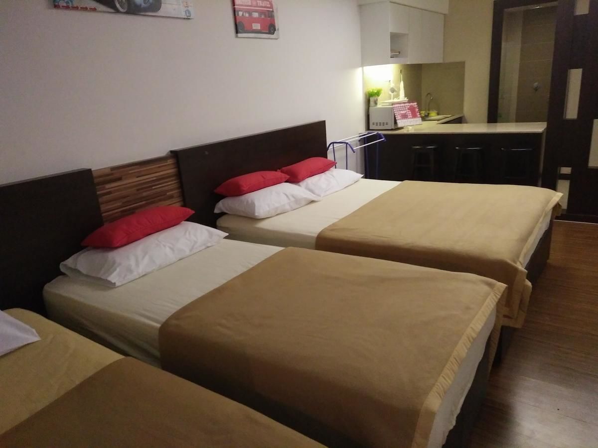 Habitación de hotel con dos camas, cada una con cabecero de madera y ropa de cama color beige. Cuenta con una pequeña zona de kitchenette, un lavamanos y un espejo.