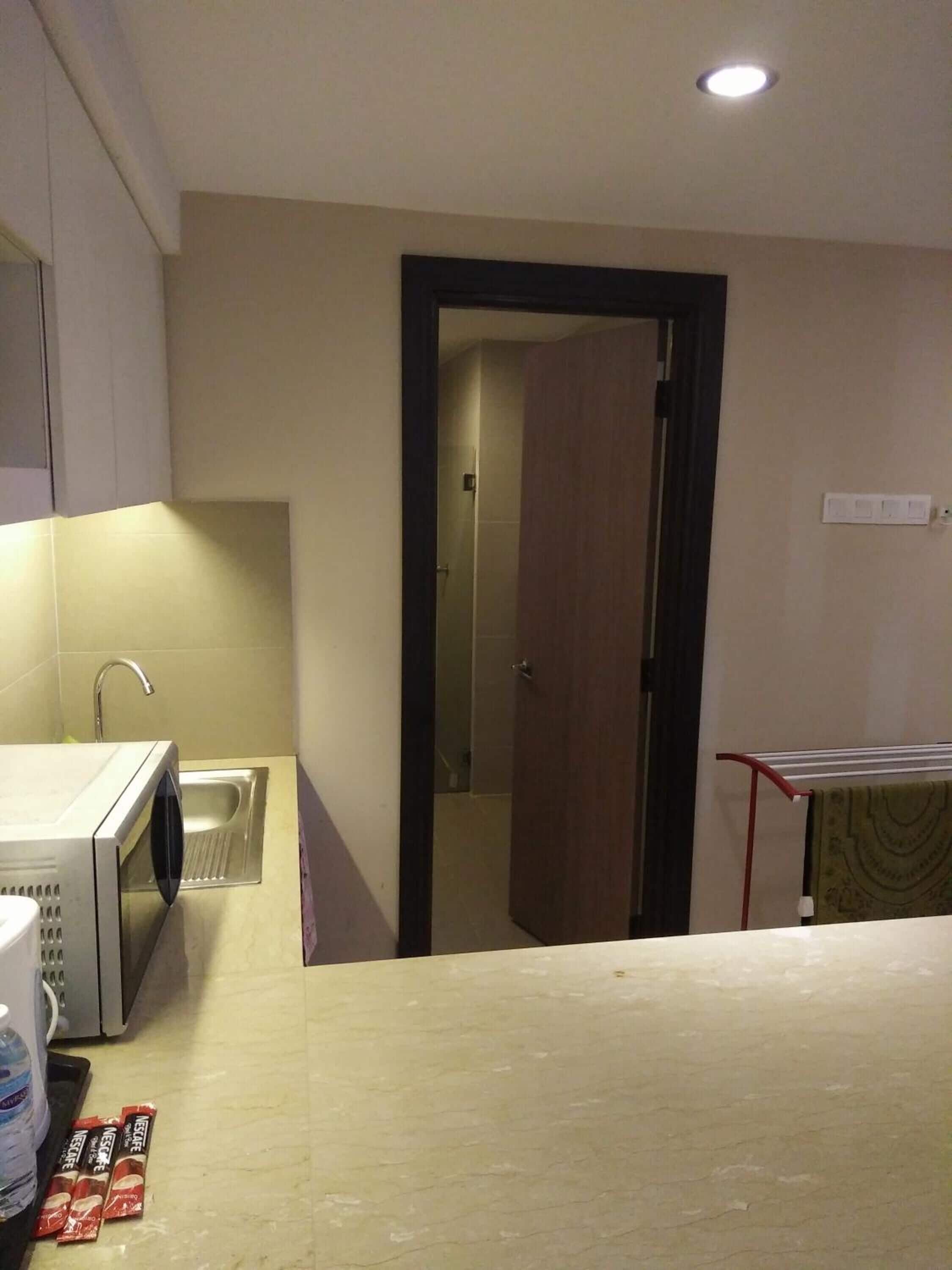 A compact kitchen with a microwave, sink, and a water dispenser. A door leads to a bathroom.