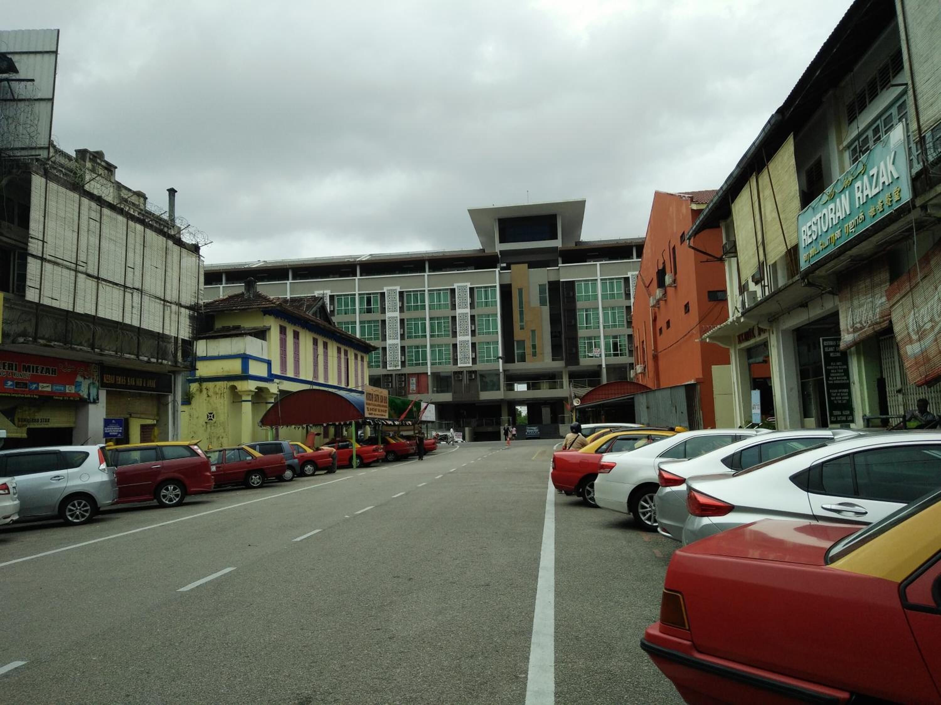 Rua com carros estacionados e edifícios, incluindo um restaurante chamado Restoran Razak.