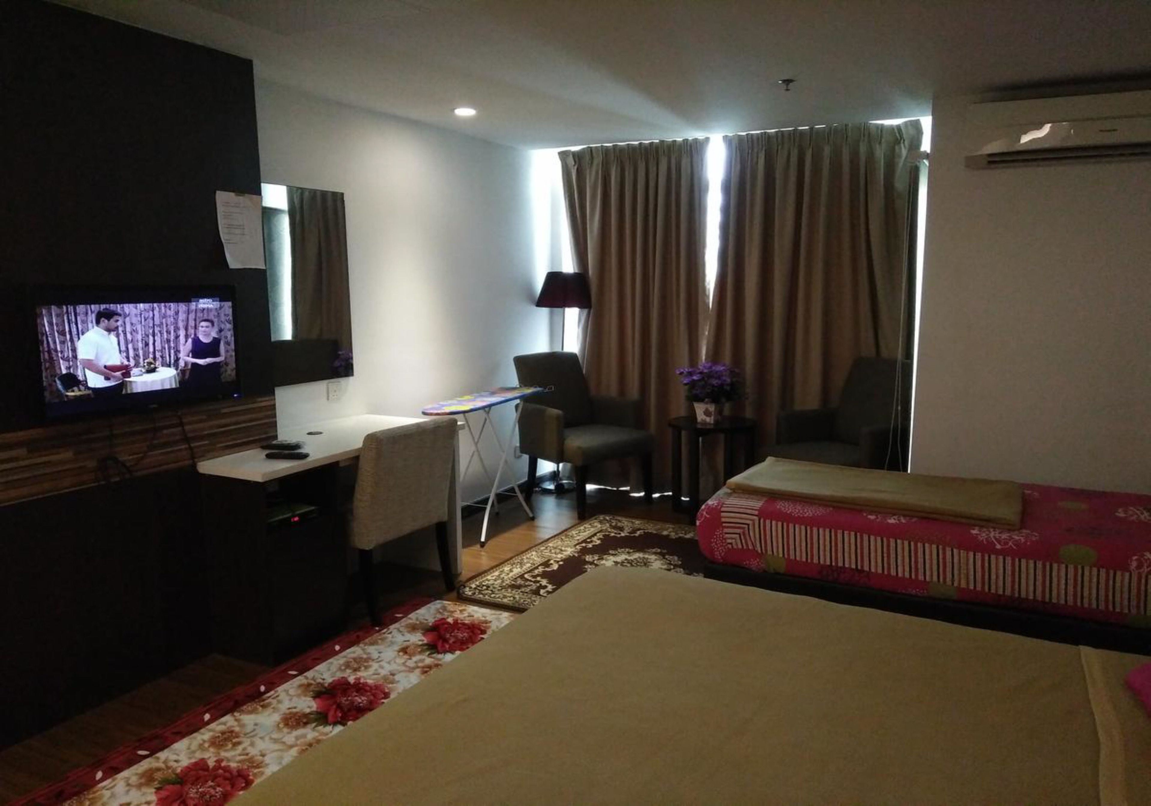 A hotel room with a bed, a desk with a chair, a television, and a window with curtains.