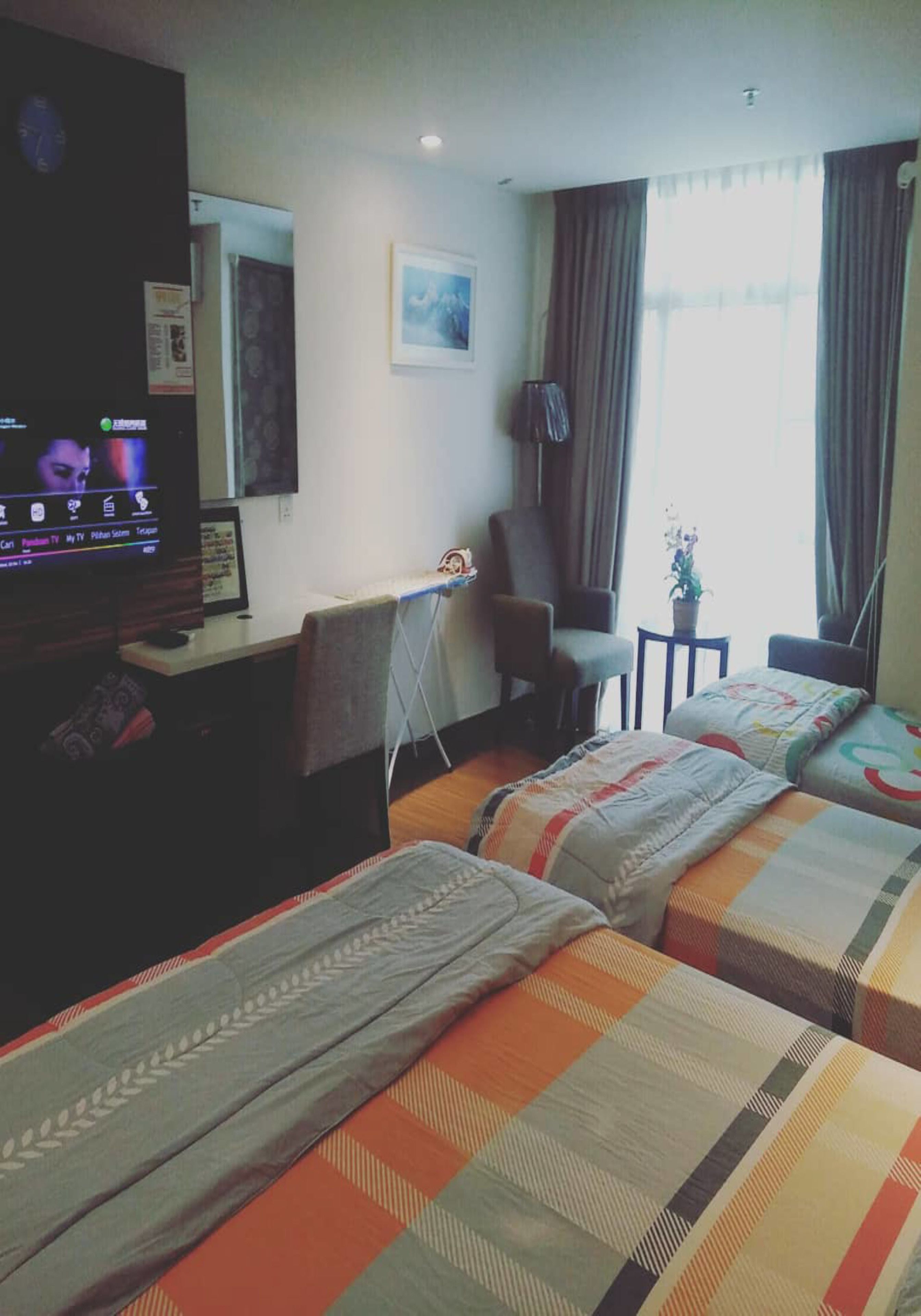 Habitación de hotel con dos camas, un escritorio, una silla, un televisor y un ventanal con cortinas.
