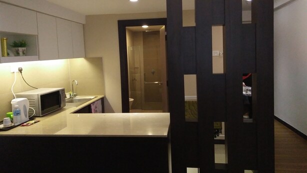 A modern kitchen with a microwave, sink, and countertop. There is a dark partition with cutouts, and a door leading to a bathroom. - Best Studio Guest House (Kota Bharu)