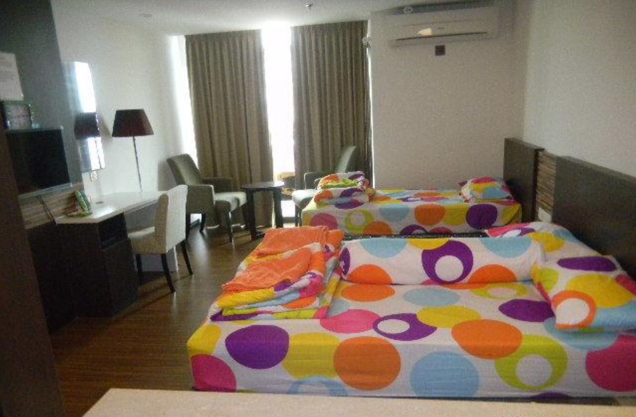 Quarto de hotel com duas camas, uma escrivaninha e uma cadeira.
