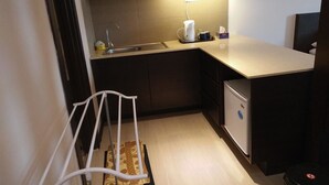 A compact kitchen with a sink, a coffee maker, a small refrigerator, and a white chair. - Best Studio Guest House (Kota Bharu)