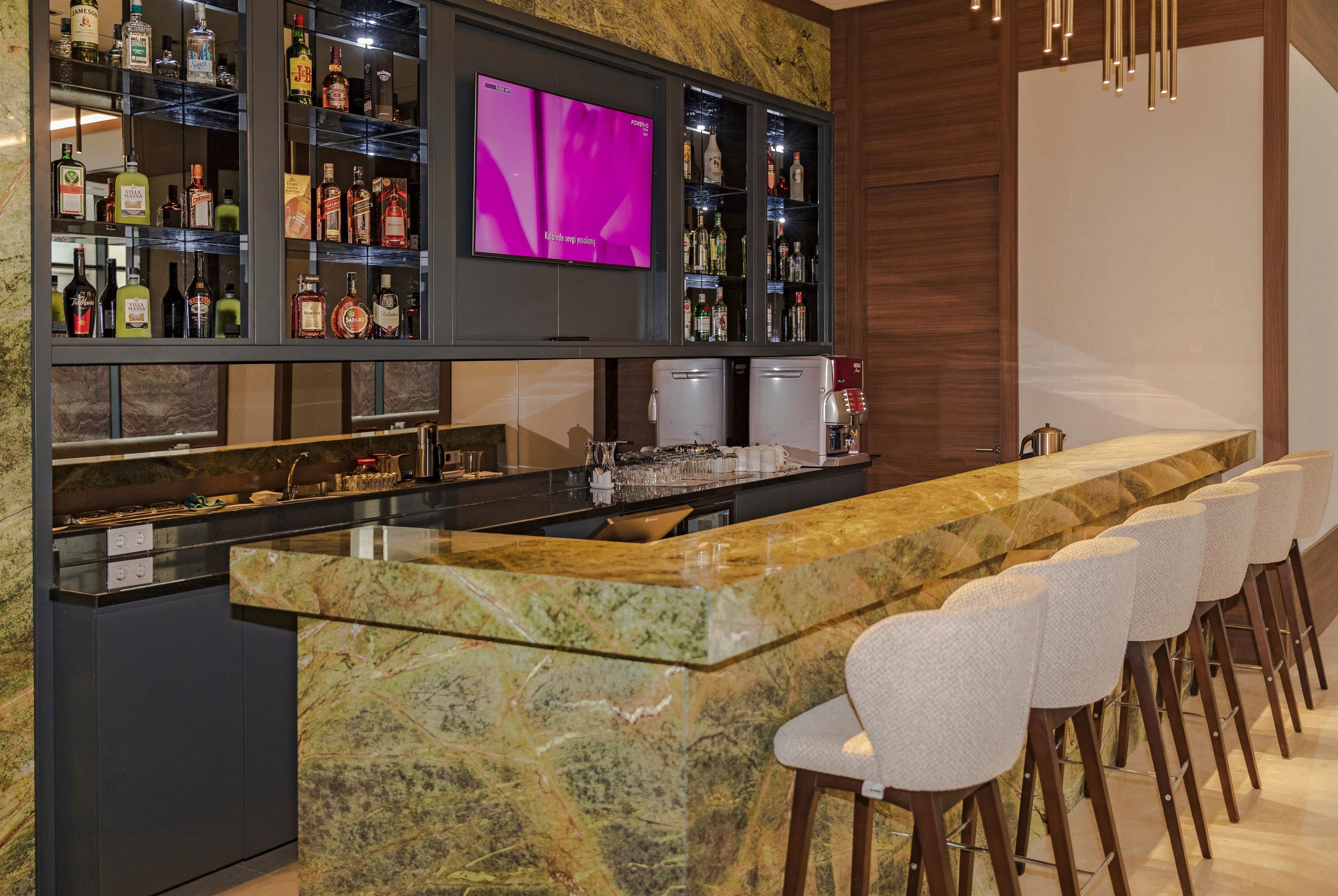 A bar area with a marble countertop, multiple liquor bottles, a television, and bar stools.