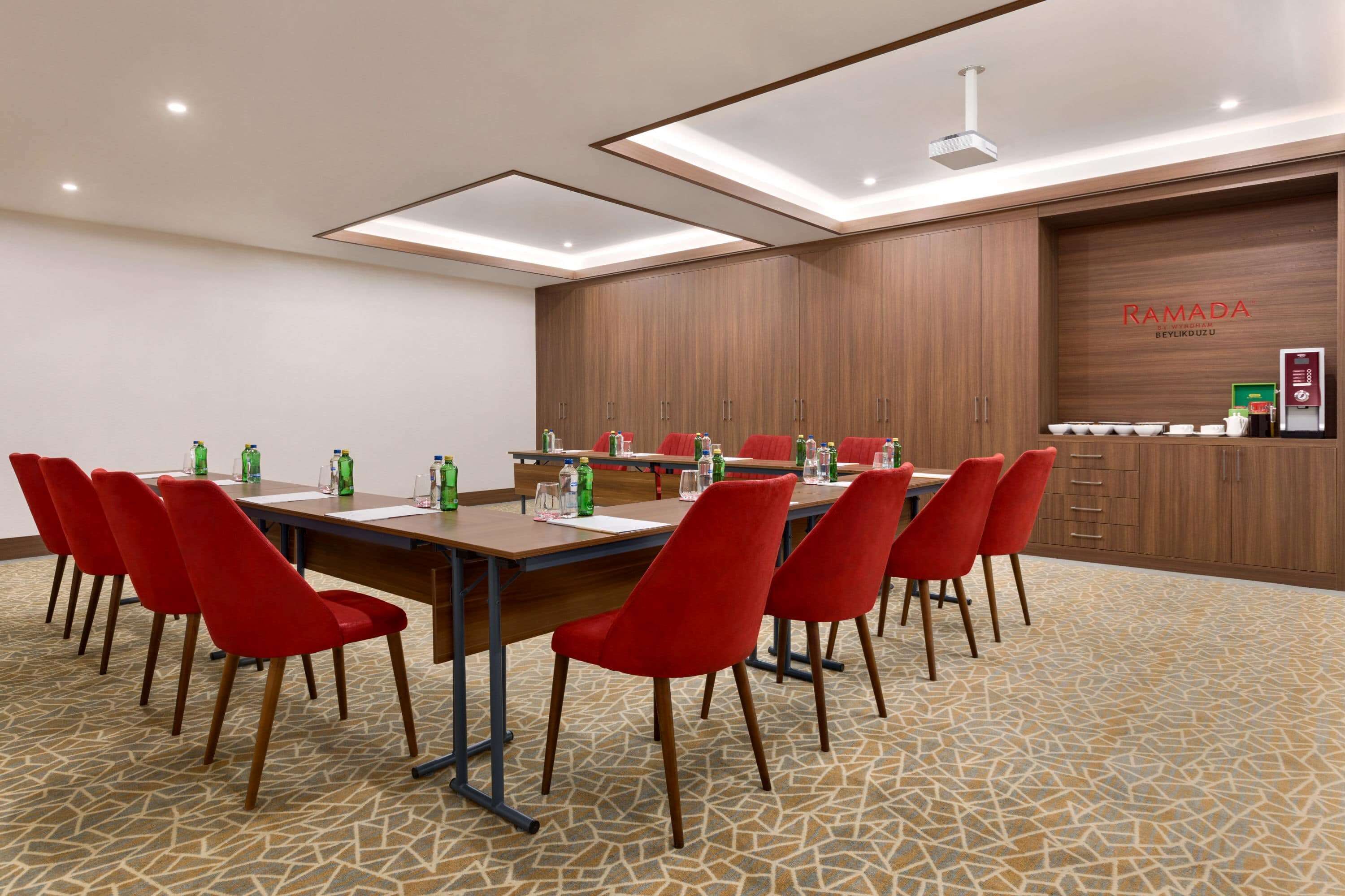 A conference room with a long table, red chairs, and a wooden cabinet with a sign.