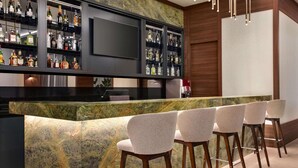 A bar area with a marble countertop, multiple liquor bottles, and four bar stools. - Ramada by Wyndham Beylikduzu (Istanbul)