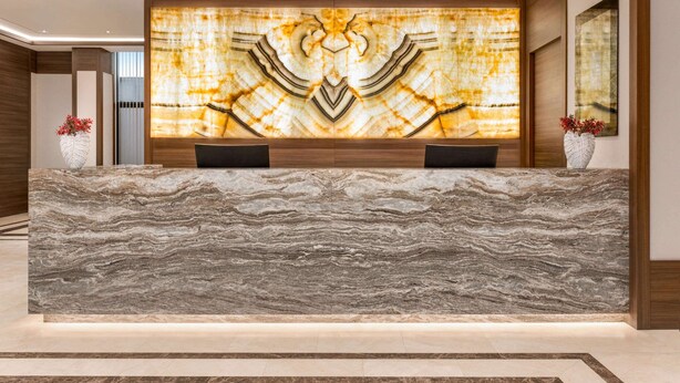 A reception desk with a marble top, two black chairs, and a large wall art piece above it. - Ramada by Wyndham Beylikduzu (Istanbul)
