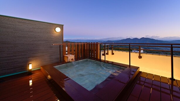 A rooftop hot tub with a wooden deck and a view of mountains in the background. - Mimatsukan (Shibukawa)
