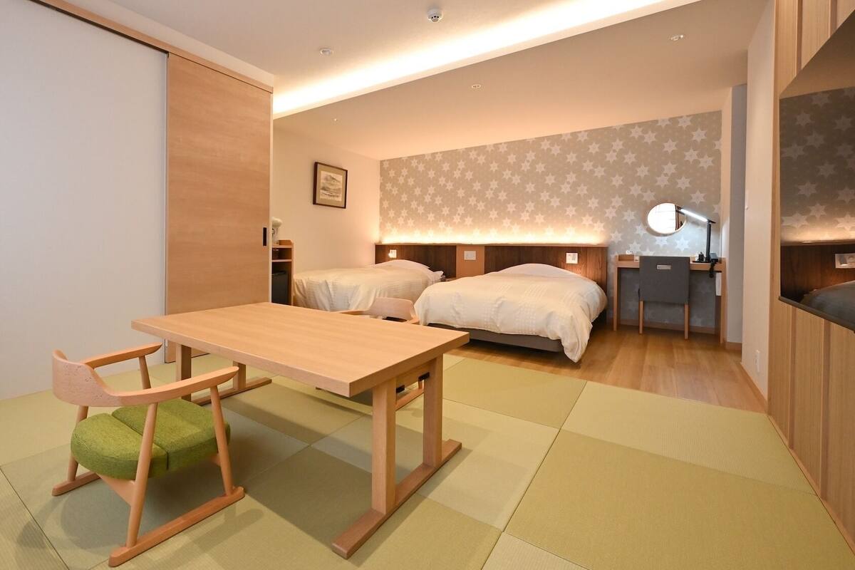 Una habitación de hotel compacta con una mesa de madera, dos camas, un escritorio y una silla.