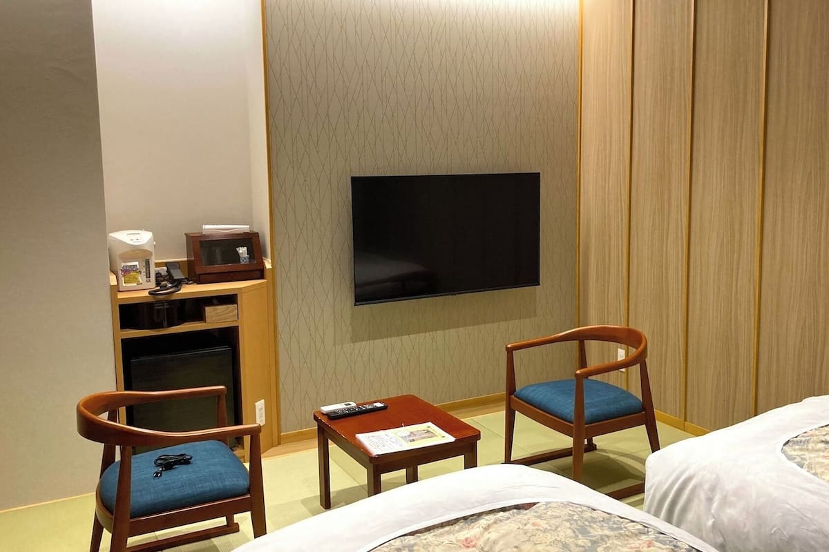 Habitación de hotel con dos camas, televisión, escritorio con lámpara y un pequeño rincón de descanso con sillas.