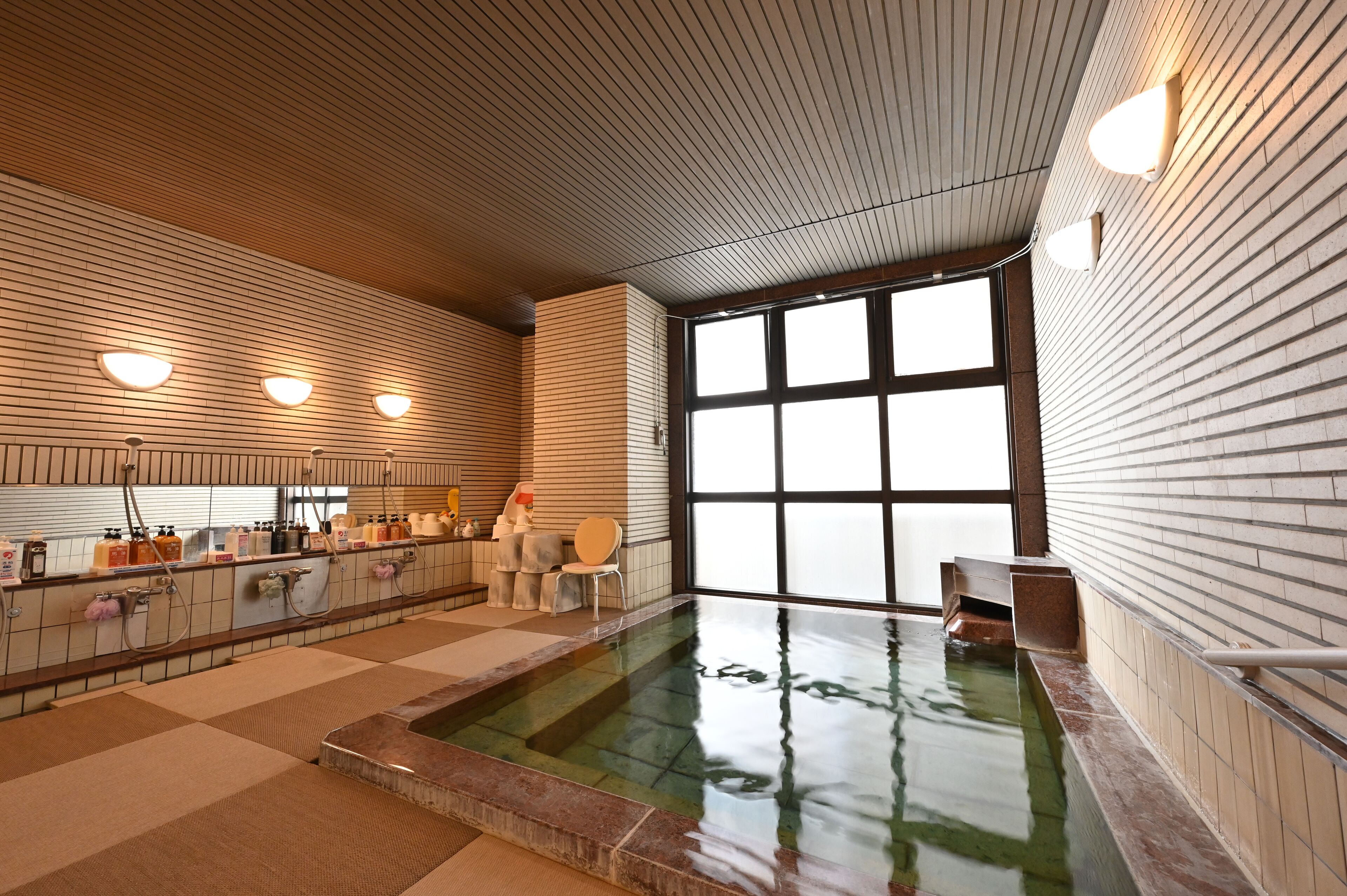 A modern indoor pool area with a checkered floor, a long counter with amenities, and large windows providing natural light.