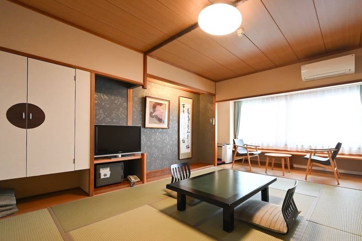 Una habitación japonesa tradicional con suelo de tatami, una mesa baja, sillas, un televisor y una puerta corredera.