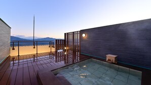 A modern rooftop terrace with a glass-enclosed hot tub, wooden deck, and a view of the mountains. - Mimatsukan (Shibukawa)