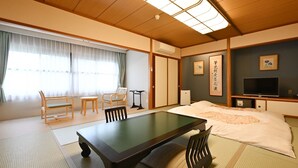 A traditional Japanese-style room with tatami flooring, a low table, a bed with a futon, a television, and a small desk. - Mimatsukan (Shibukawa)