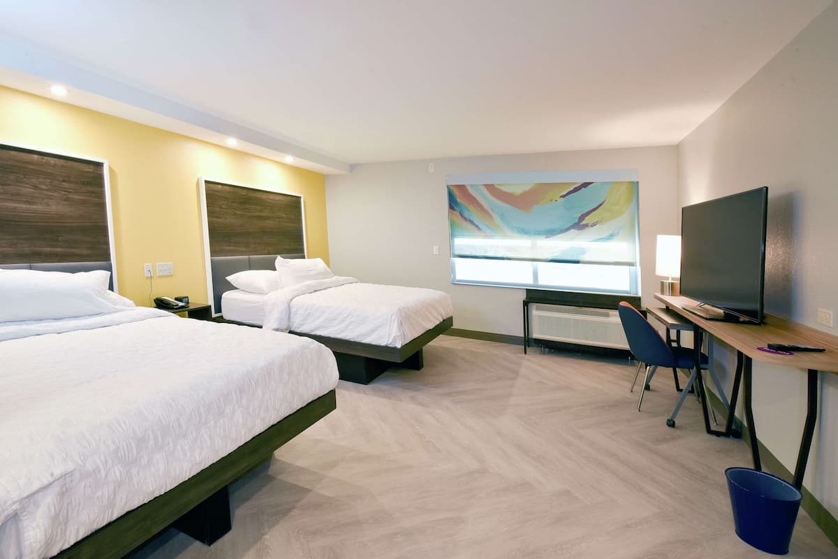 A hotel room with two beds, a desk with a computer, a TV, and a large window.