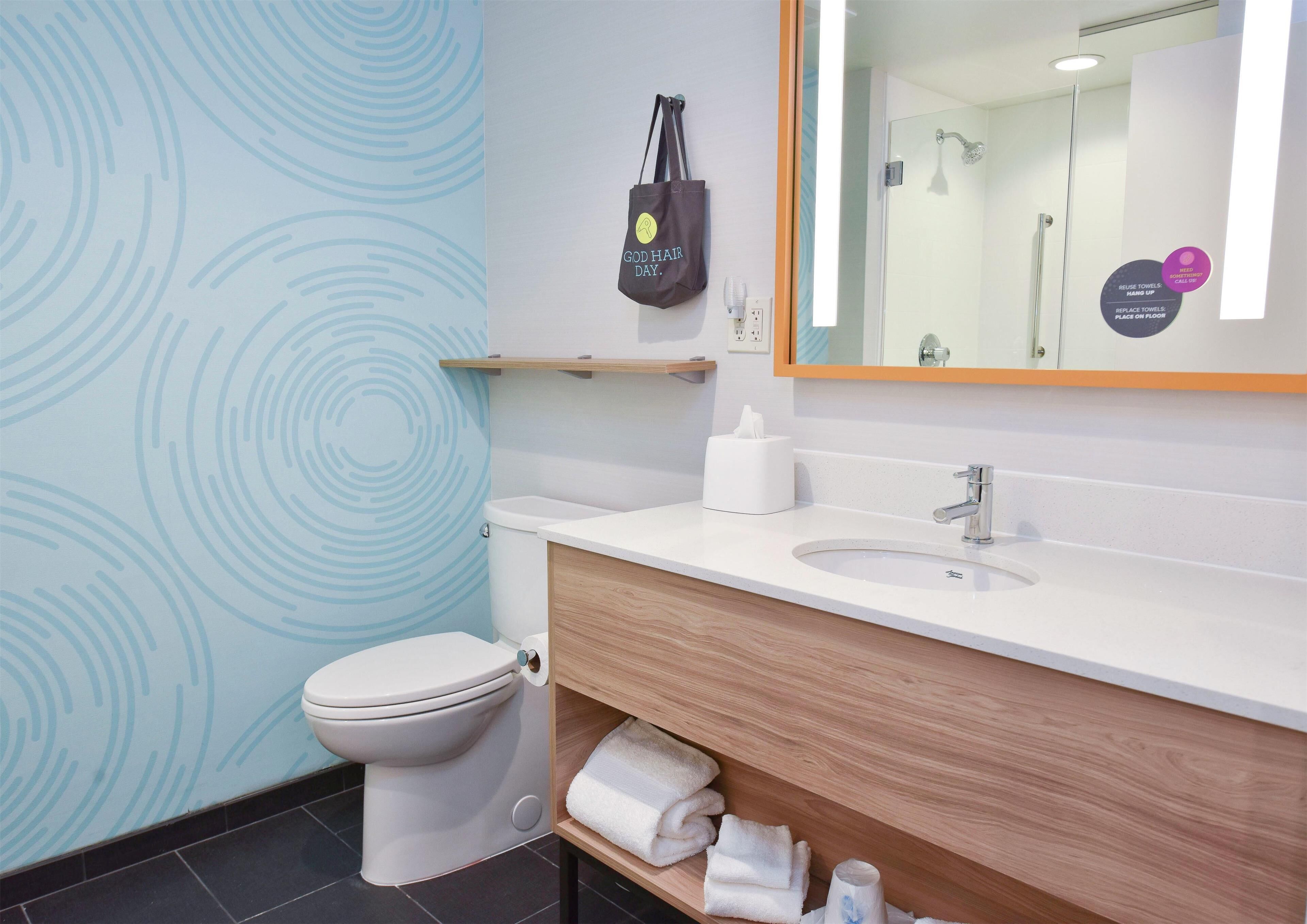 A modern bathroom with a toilet, sink, and mirror. There is a towel rack with towels and a bag hanging on the wall.