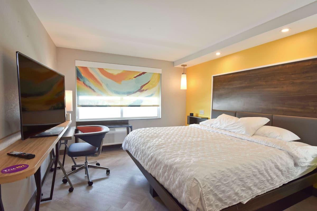 A hotel room with a bed, a desk with a computer, a chair, a TV, and a large window.
