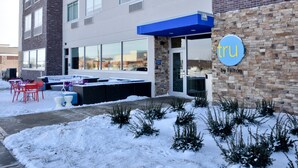 Een hotelgevel met een blauw afdak, een terras en een met sneeuw bedekte grond.