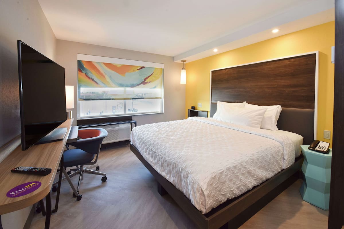 A hotel room with a bed, a desk with a computer, a TV, and a painting on the wall.