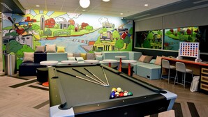 Een pooltafel met keuen en ballen, een muurschildering van een stadsbeeld, en zithoeken met tafels en stoelen.