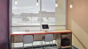 A modern office space with a desk, two chairs, a computer monitor, and a window with a view of a snowy parking lot.