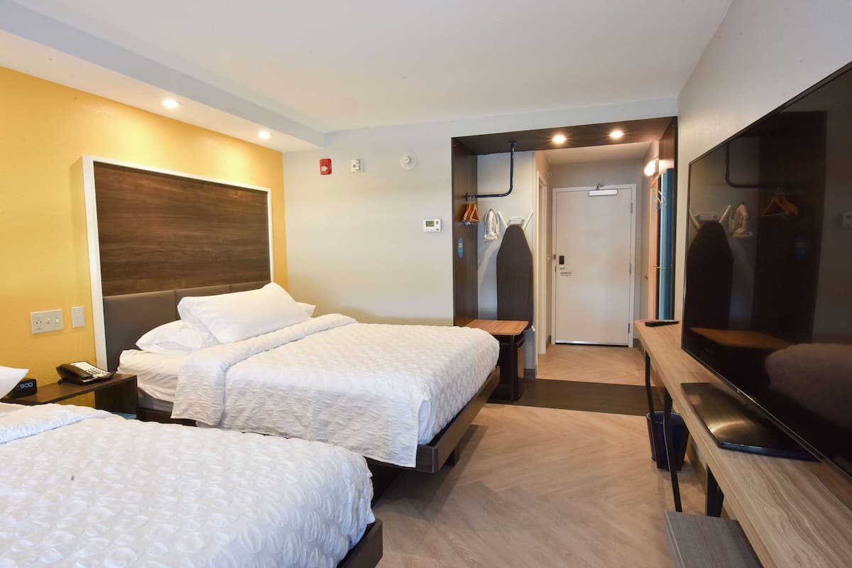 A hotel room with two beds, a TV, a wardrobe, and a bathroom visible through an open door.