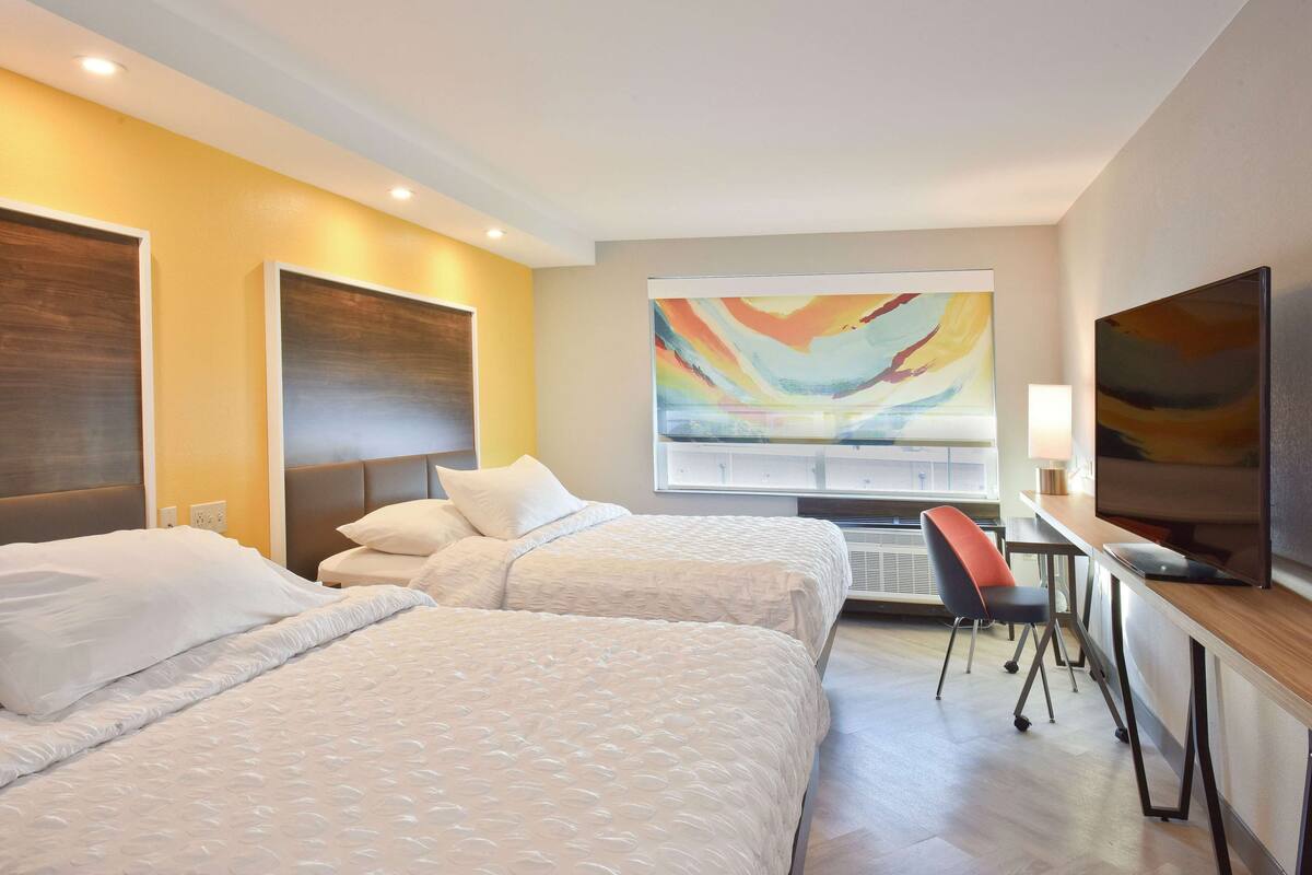A hotel room with two beds, a desk, a chair, a television, and a large abstract painting on the wall.