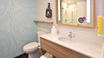 A modern bathroom with a toilet, sink, and mirror. There is a towel rack and a shelf with a bag.