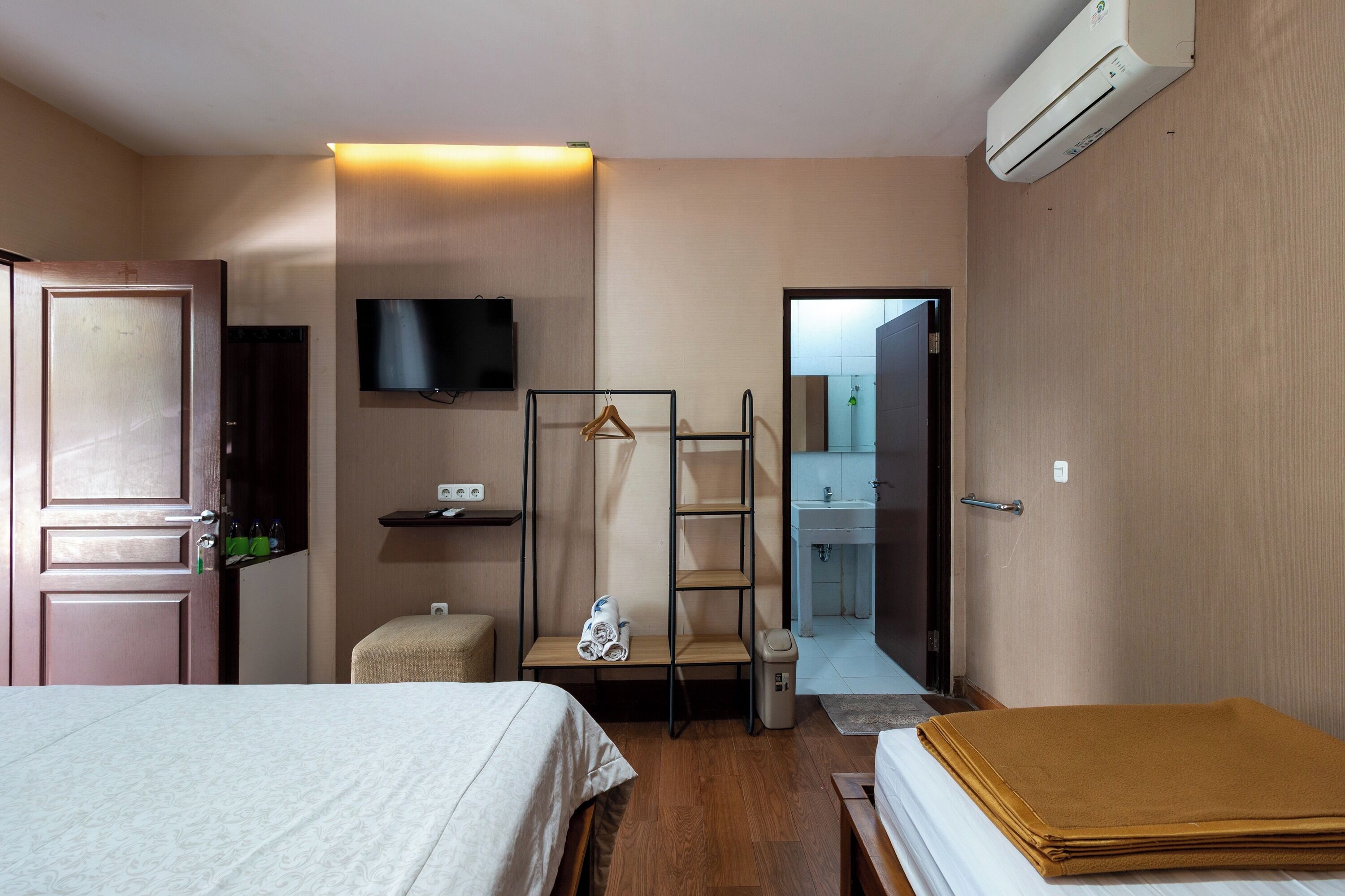 A hotel room with a bed, a desk, a chair, a TV, and a bathroom visible through an open door.
