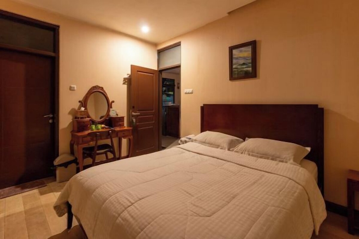 A hotel room with a large bed, a wooden dresser, a mirror, and a painting on the wall.