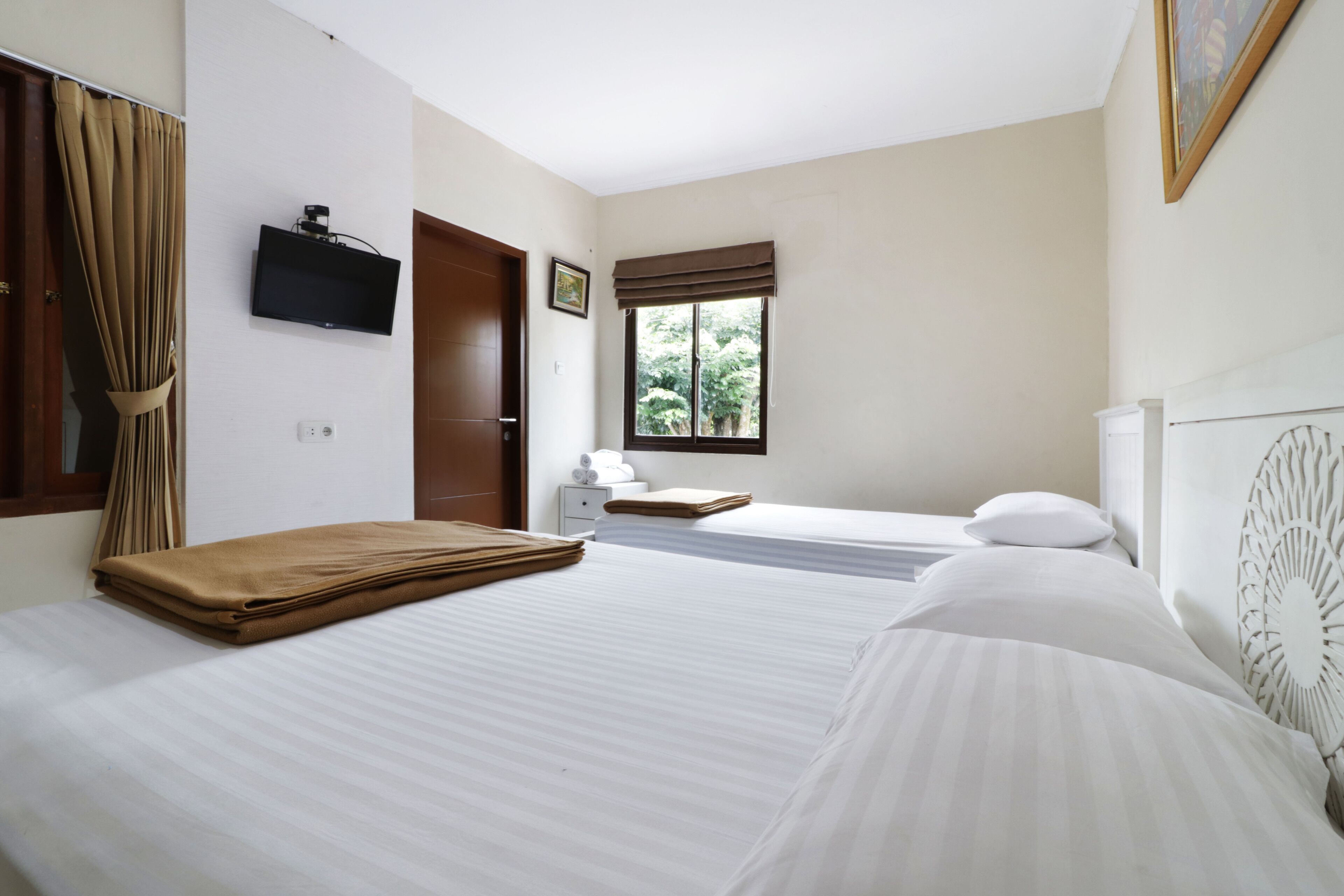 Habitación de hotel con dos camas, un televisor, una ventana con vistas a zonas verdes y un cuadro en la pared.