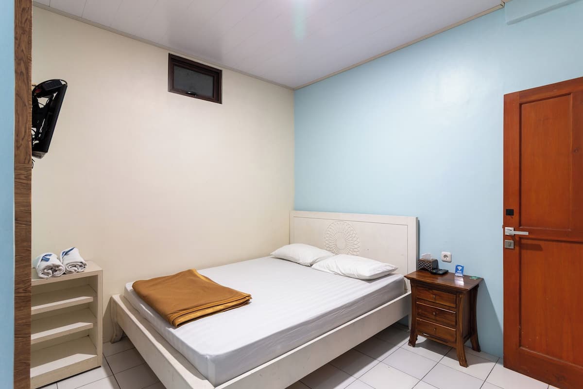 A bedroom with a bed, a nightstand, a wooden door, and a wall-mounted TV.