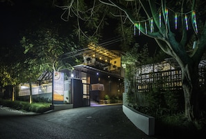 A modern building with a covered entrance, a gated driveway, and a well-lit facade at night. - Jayagiri Guesthouse By Belgareti (Lembang)