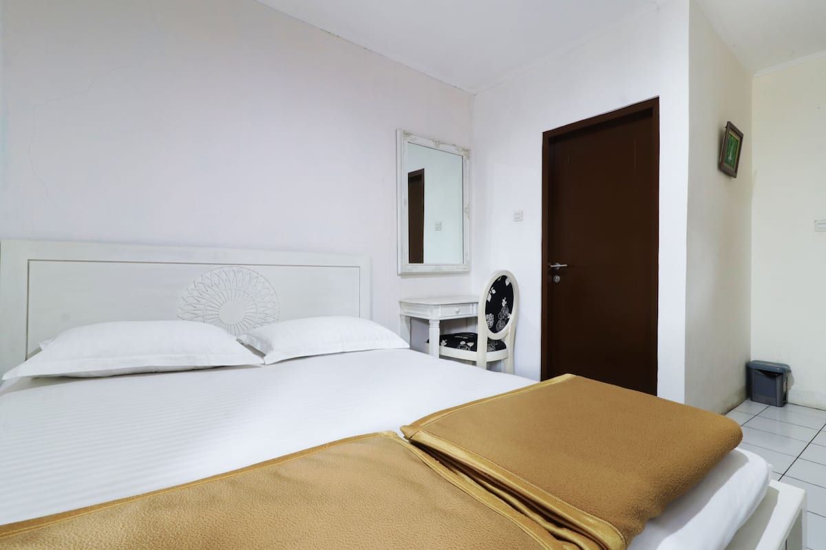 A hotel room with a bed, a bedside table, a chair, a door, and a small trash bin.