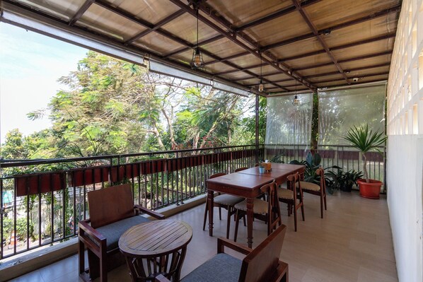 A covered outdoor seating area with wooden furniture, a view of greenery, and a metal railing. - Jayagiri Guesthouse By Belgareti (Lembang)