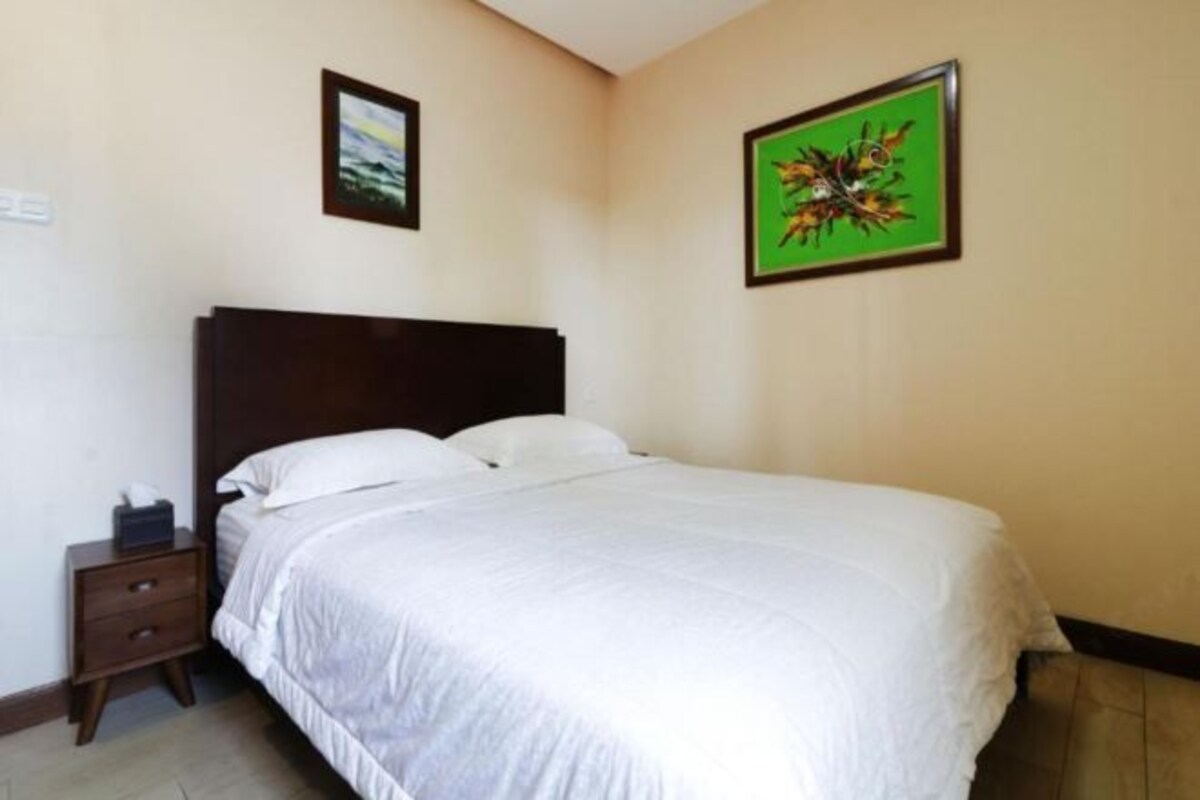 A neatly made bed with white bedding in a room with cream walls.