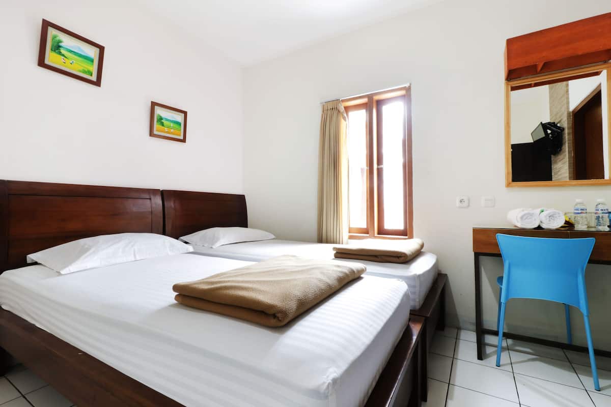 A hotel room with a wooden bed, white linens, a blue chair, a desk with toiletries, and two framed pictures on the wall.