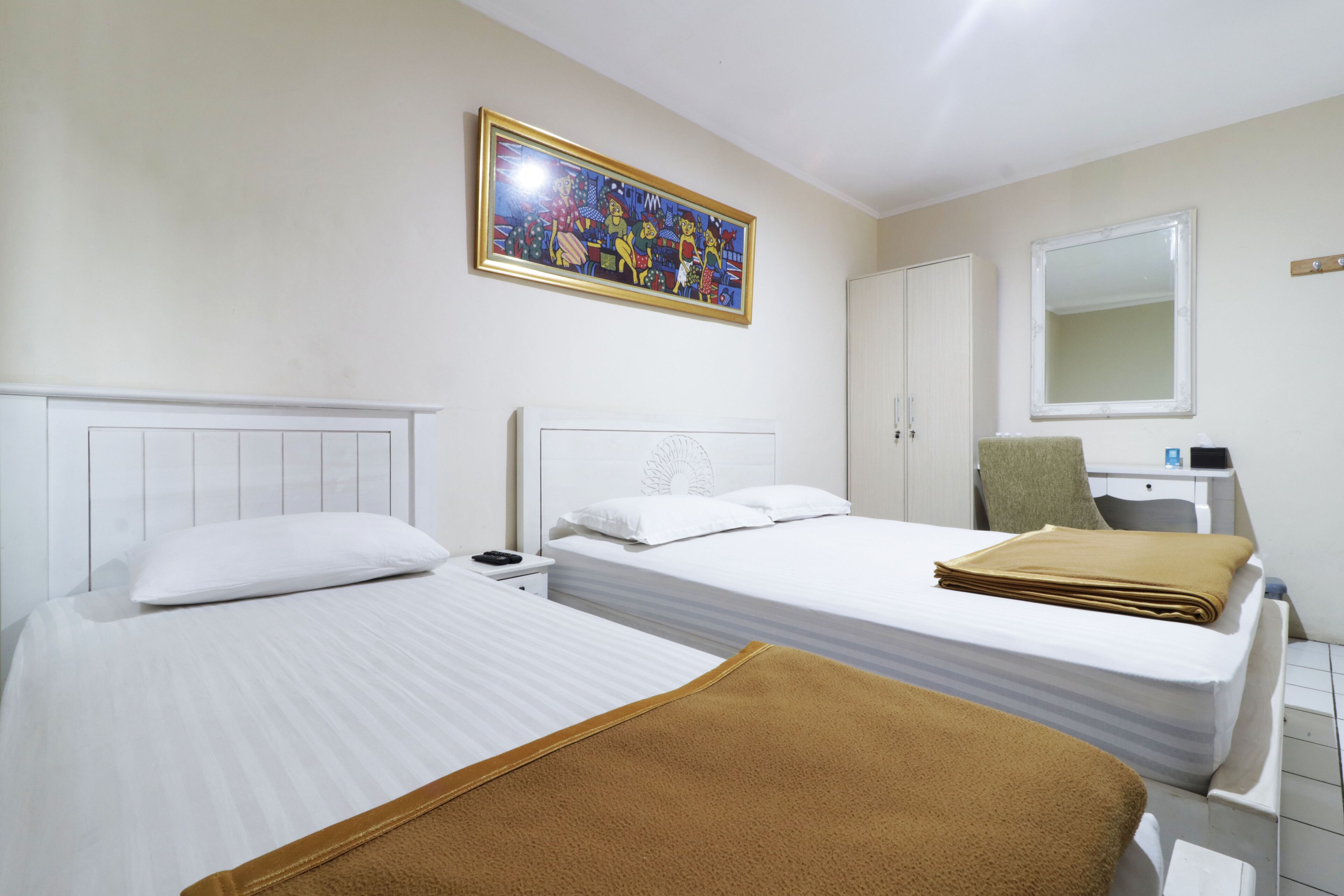 A hotel room with two beds, a painting on the wall, a desk with a chair, and a mirror.